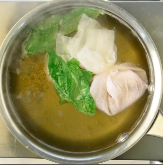 A bag of spices and basil simmering in water