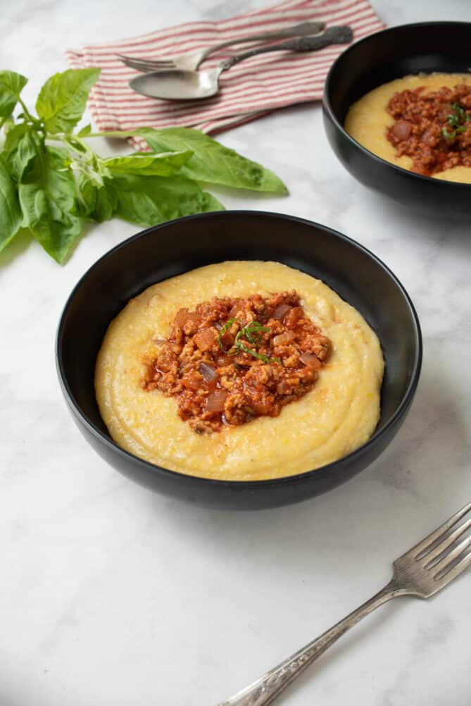 A black bowl with creamy polenta and Italian sauce tomato sauce