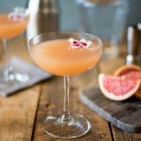 A stemmed glass of April Showers cocktail garnished with an edible flower