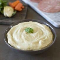 Artichoke cream in a bowl with fresh artichokes behind