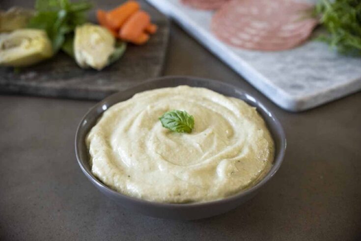 Artichoke cream in a bowl with fresh artichokes behind