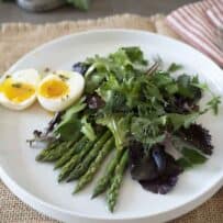 Green and purple salad on a round plate with asparagus and egg
