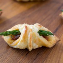 An asparagus sun-dried tomato puff pastry bite on a board