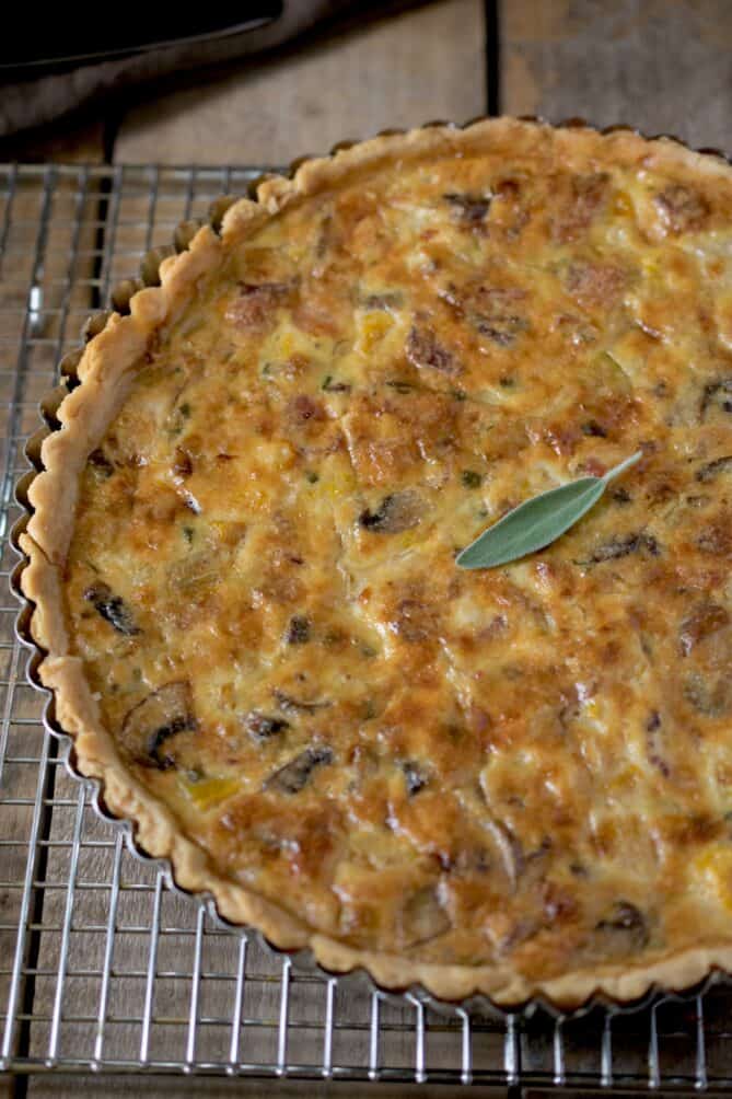 A closeup of a vegetable quiche topped with a sage leaf in the center
