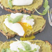 A poached egg on avocado artichoke toast cut open with yolk running out
