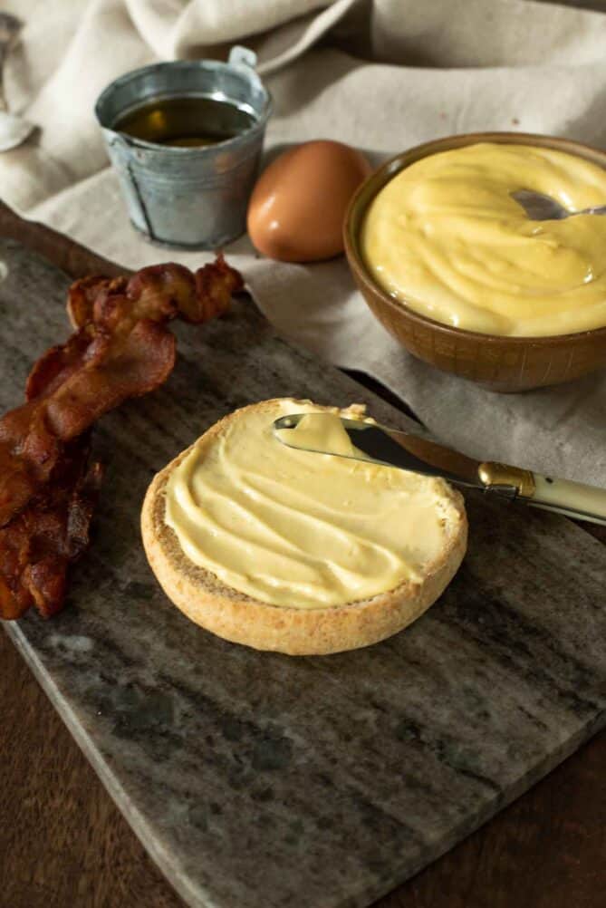 A bun topped with mayonnaise with slices of bacon