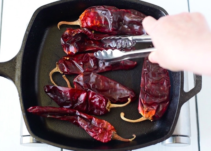 Dried guajillo peppers toasting in a cast iron skillet