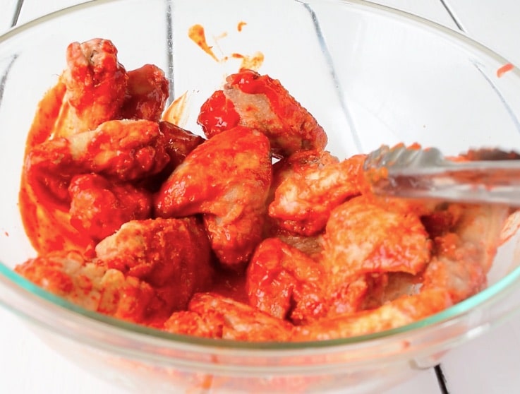 Crispy wings in a glass bowl being coated in a adobo sauce