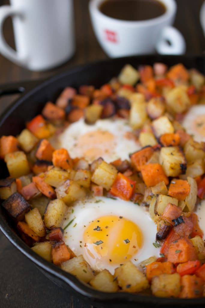 Russet and sweet potatoes are browned in a cast iron skillet with sunny side up eggs