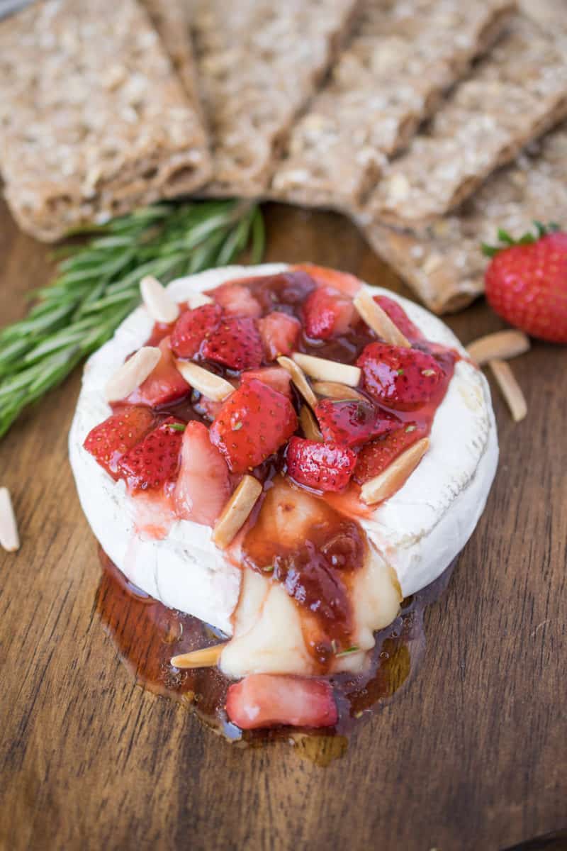 A wheel of brie with melted cheese oozing out topped with strawberries