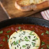 A closeup of a round of goat cheese coated with herbs siting in marinara sauce