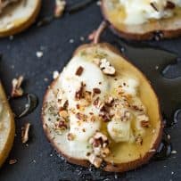 A closeup of a baked pear slice with melted goat cheese, honey and pecans