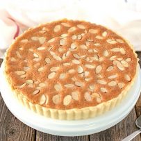 A whole bakewell tart on a cake stand ready to be sliced