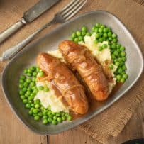 Bangers and mash with onion gravy and peas on a grey plate