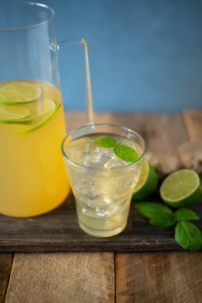 A pitcher and a glass of herbal tea with fresh limes and basil