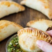 A beef and mushroom empanada being dipped into chimichurri sauce