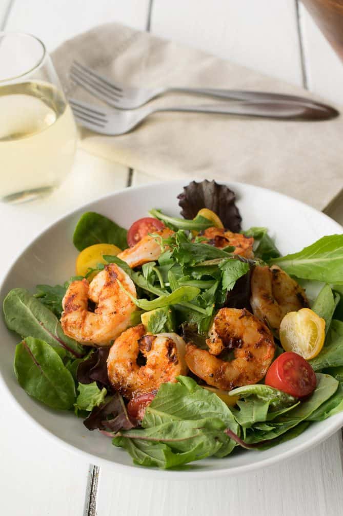 Lettuce, tomatoes, and grilled shrimp on a white plate