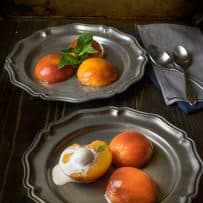 3 poached peach halves on pewter plates one topped with ice cream