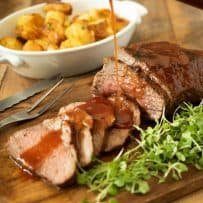 Drizzling barbecue sauce over sliced Tri tip with roast potatoes in the background