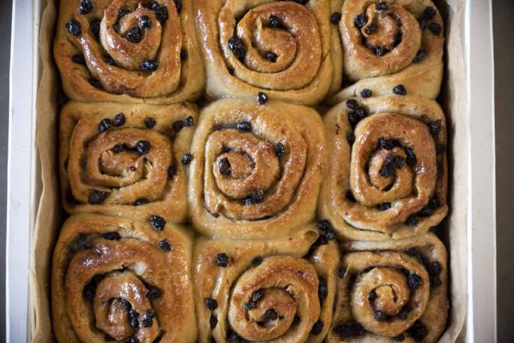 9 browned Chelsea buns dotted with dried currants in right out of the oven