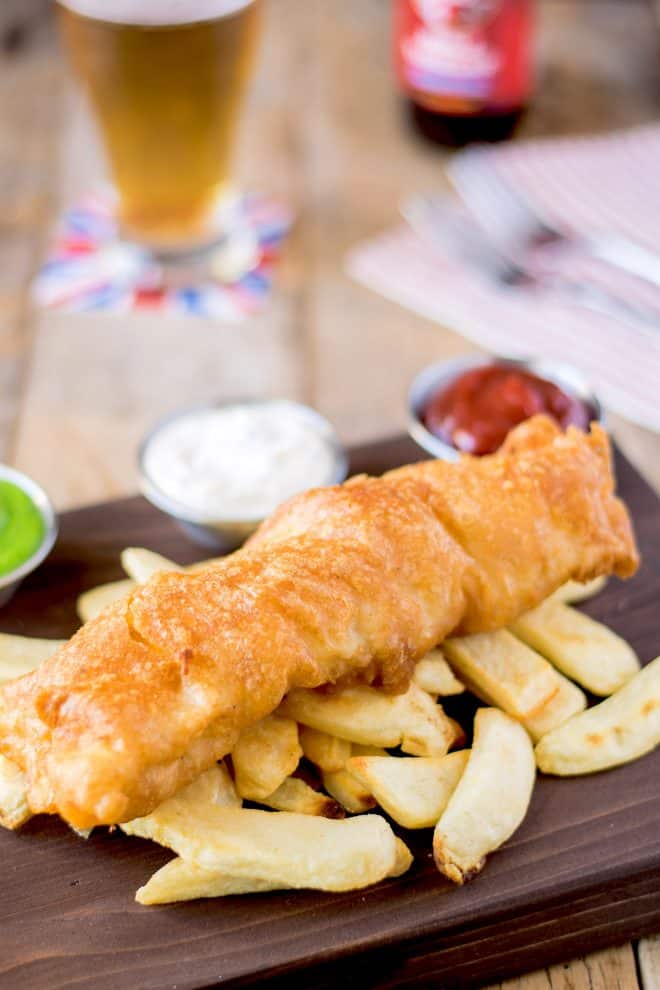 A battered piece of cod fish sitting on top of chips/French fries
