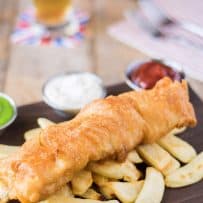 A large piece of fried cod laying on top of chips/French fries