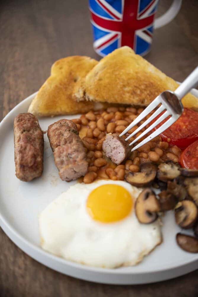 A piece of sausage on a fork with a plate of breakfast items