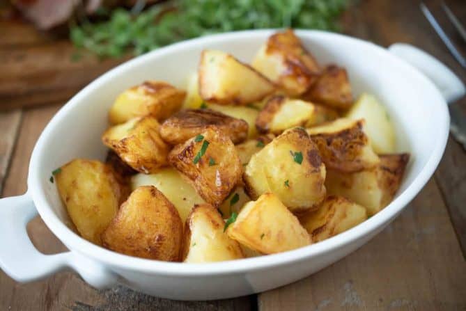 An white oval serving bowl filled with roasted potatoes
