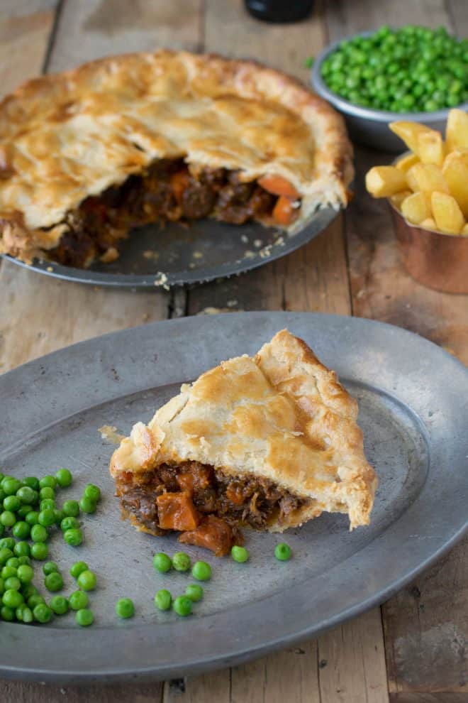 A slice of steak and ale pie on a plate with peas