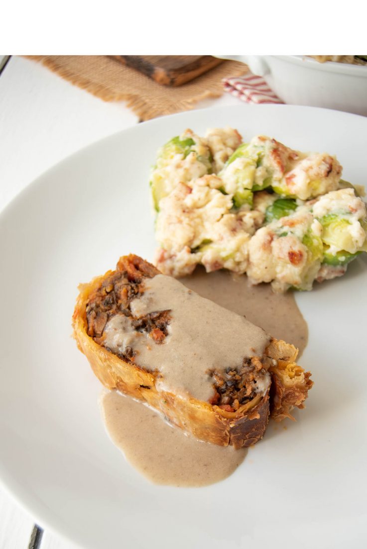 A slice a of mushroom wellington and brussels sprouts and bacon gratin on a white plate