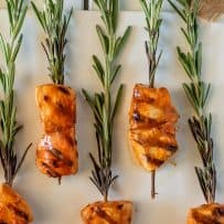 Rows of grilled buffalo chicken threaded onto fresh rosemary sprigs