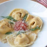 Fresh pasta folded into cappellacci shape to look like nuns hats with brown butter, crispy sage, red pasta sauce and grated Parmesan cheese
