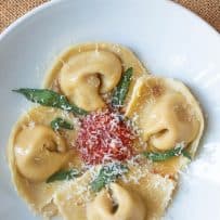 Stuffed pasta on a white plate with crispy sage leaves and a little marinara sauce in the center