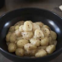A black bowl filled with potato gnocchi in a cacio e pepe sauce