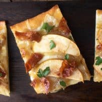 A rectangle shaped piece of flatbread with 2 apple slices, crispy bacon bits and chopped parsley