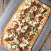 A caramelized onion apple and bacon flatbread pizza from overhead on a baking sheet shaped in a long rectangle