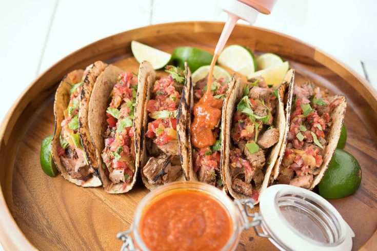 Carne asada tacos being topped with bbq sauce