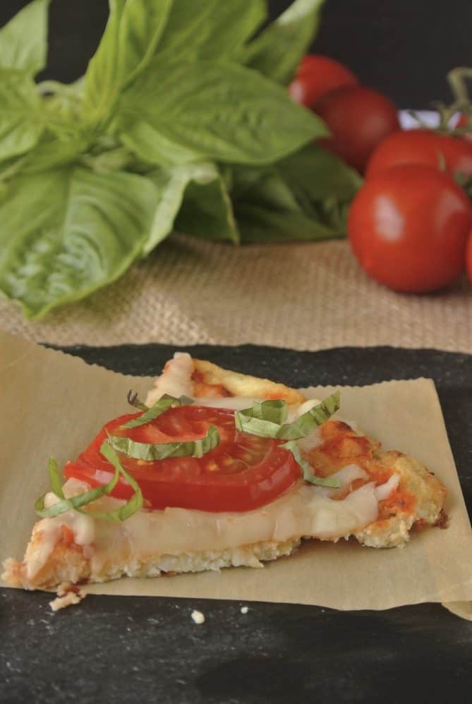 A slice of cauliflower crust pizza topped with cheese, tomato and basil