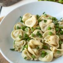 A closeup of tortellini topped with peas and chopped parsley