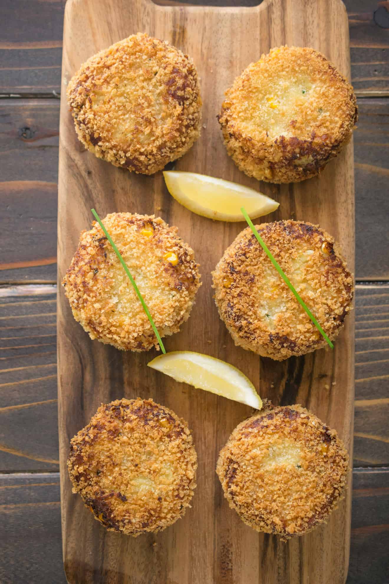 5 cheesy tuna melt cakes on a serving board with lemon wedges and chives