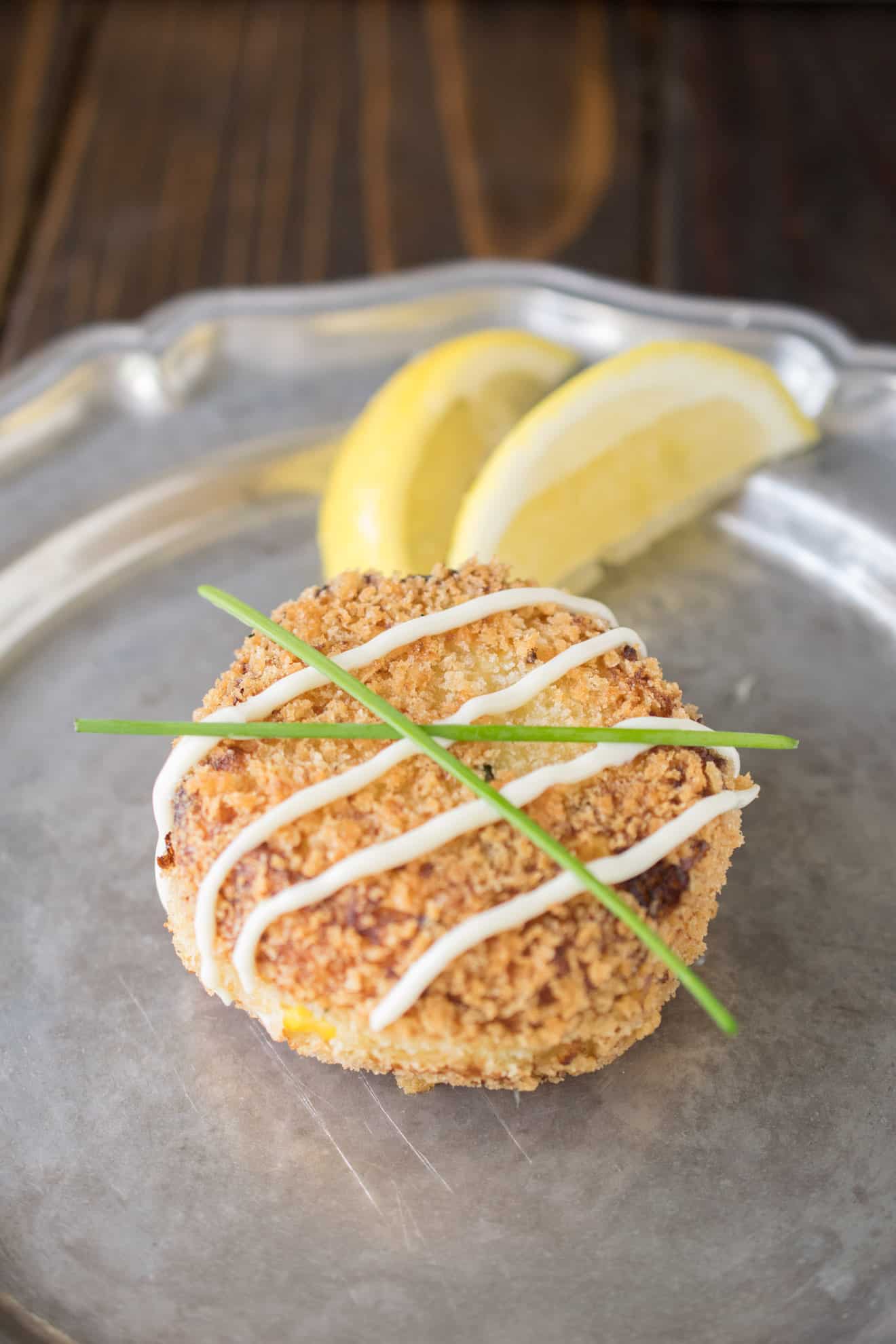 A cheesy tuna melt cake on a plate with a drizzle, chives and lemon