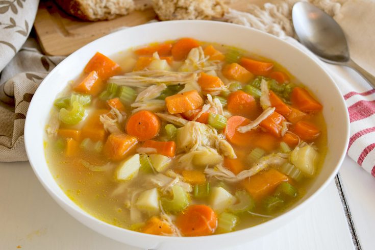 The best chicken soup served in a white bowl with a napkin, spoon and bread