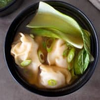 A black bowl with chicken wontons, bok choy and broth
