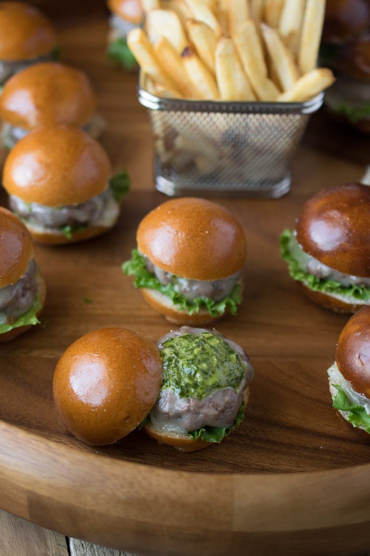 A closeup of a burger bite with the top removed showing the green chimichurri