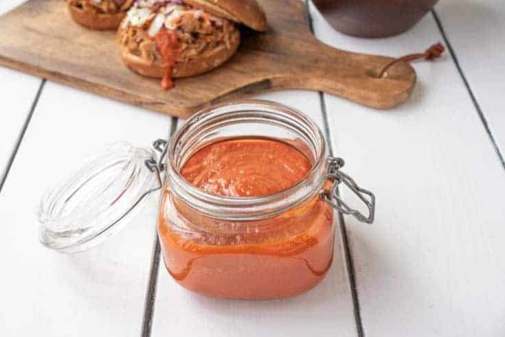 A jar full of bbq sauce with a pulled pork sandwich