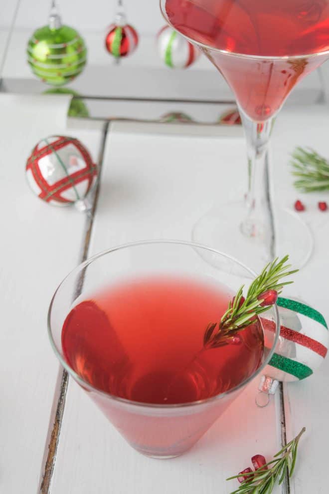 A Christmas Cosmopolitan in a short glass and one in a martini glass with holiday decorations