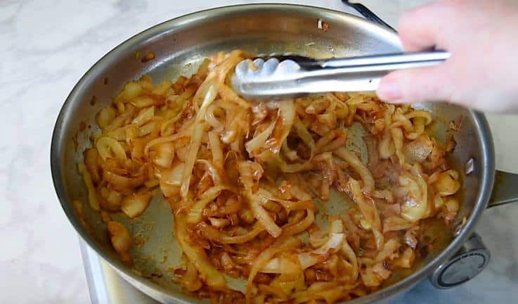 A pan of sweet, browned caramelized onions being mixed with tongs