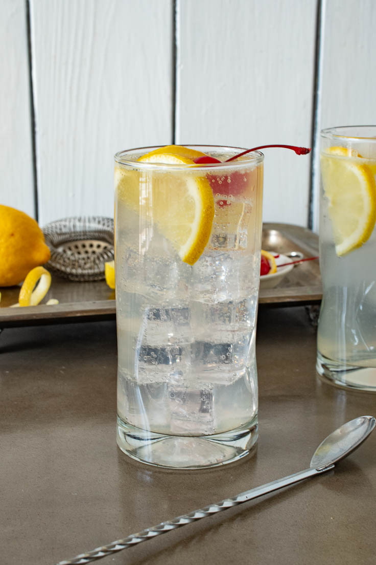 A glass of Tom Collins from the side with a serving tray