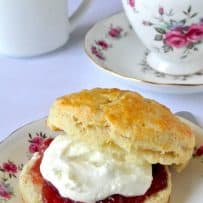 An English scone on a floured China plate spread with strawberry jam and clotted cream