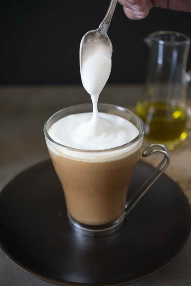 A cup of iced coffee in a glass mug topped with foamed milk